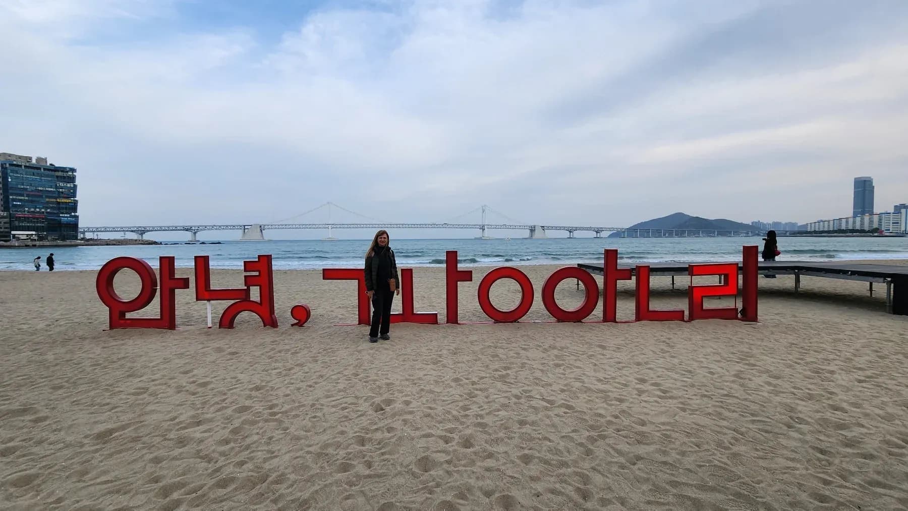 Viajera de Korea Tour junto al cartel de la playa de Gwangalli, en Busan, con el puente Gwangan de fondo