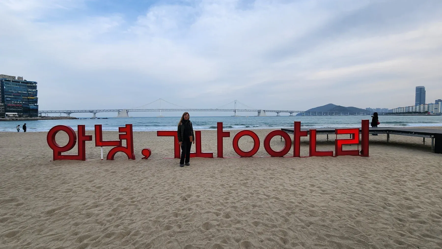 Viajera de Korea Tour junto al cartel de la playa de Gwangalli, en Busan, con el puente Gwangan de fondo